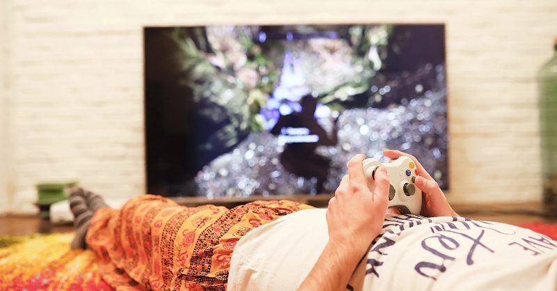Dailyza: Why Gaming Is the Modern Antidote to Daily Stress A person relaxing while playing a video game on a console in a modern living room.